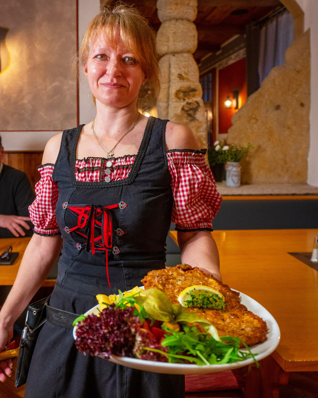 Gaststätte Schrammsteinbaude – Regionale Küche – Lecker Schnitzel Eine Frau im Dirndl trägt einen Teller mit einem lecker aussehenden Schnitzel und allerhand Beilagen