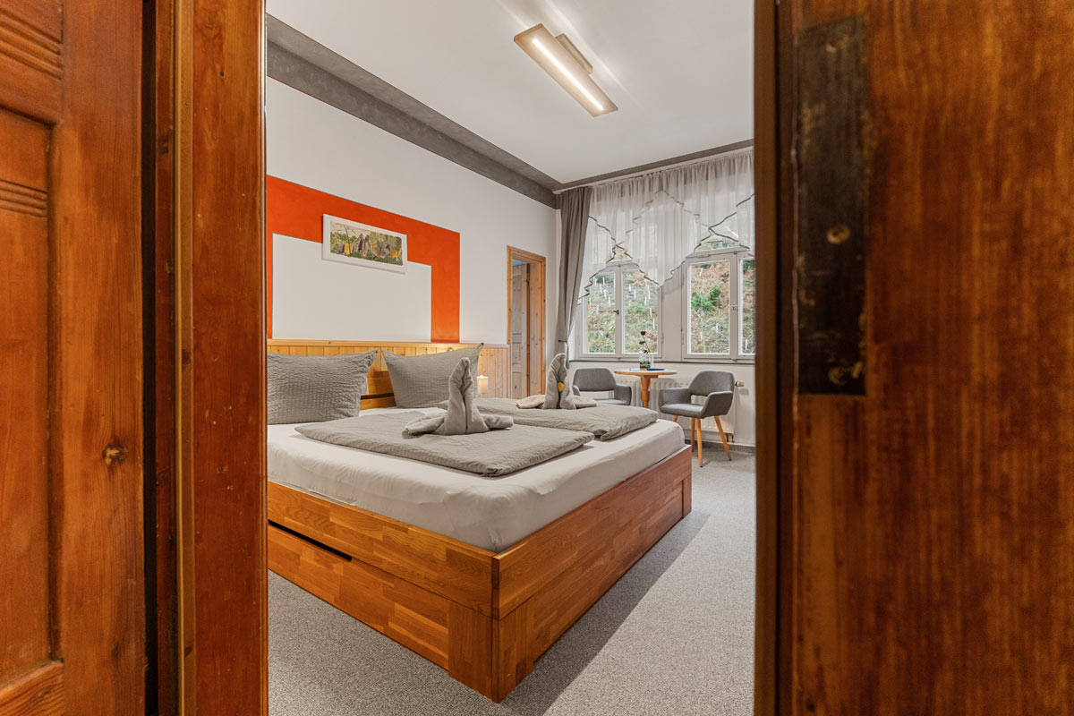 Blick in ein helles Zimmer mit Naturholzoptik, Doppelbett, Sitzgelegenheit und Blick ins Grüne.