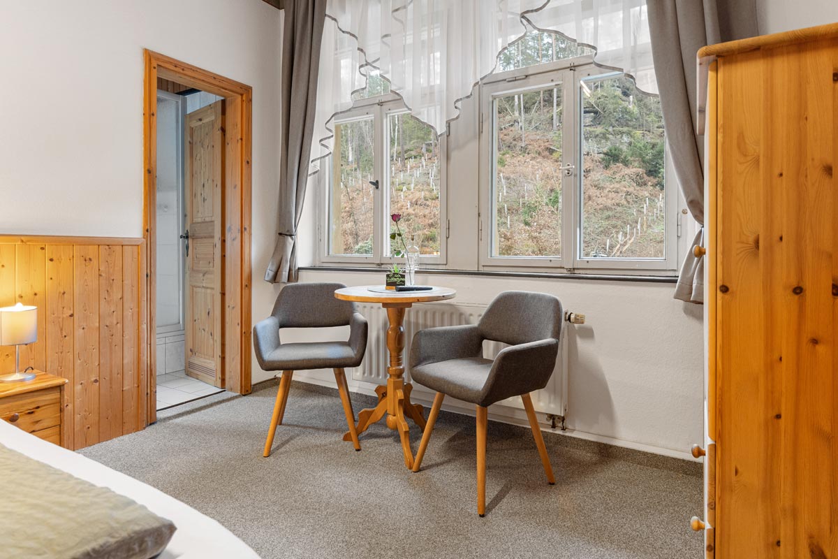 Blick in ein helles Zimmer mit Naturholzoptik, Sitzgelegenheit und Blick ins Grüne.