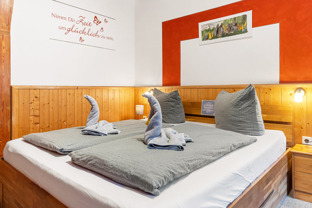 Blick in ein helles Zimmer mit Naturholzoptik, Doppelbett und Wandbild und -spruch.