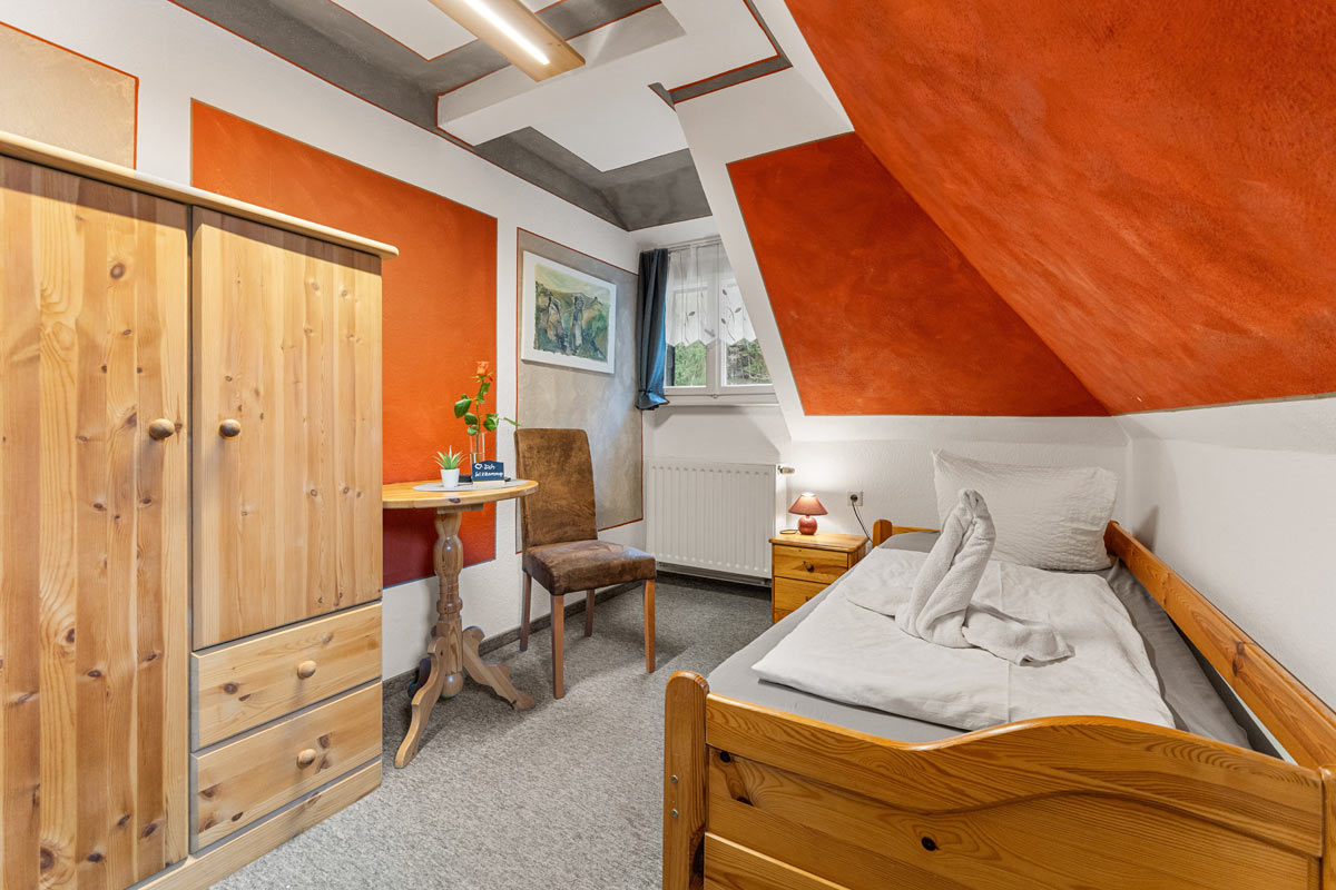 Pension Schrammsteinbaude – Einzelzimmer mit Kleiderschrank Blick in ein Einzelzimmer mit Naturholzoptik, Bett, Sitzgelegenheit und Kleiderschrank.