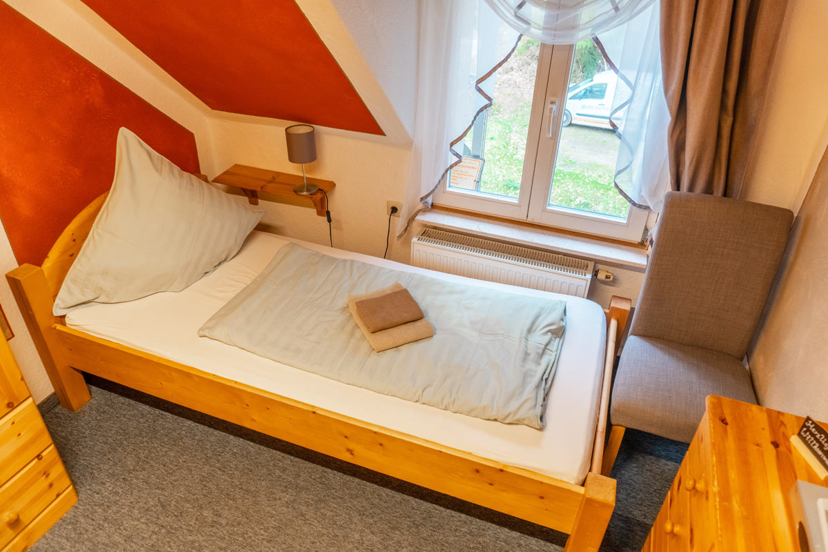 Blick in ein Einzelzimmer mit Naturholzoptik, Bett und Sitzgelegenheit.