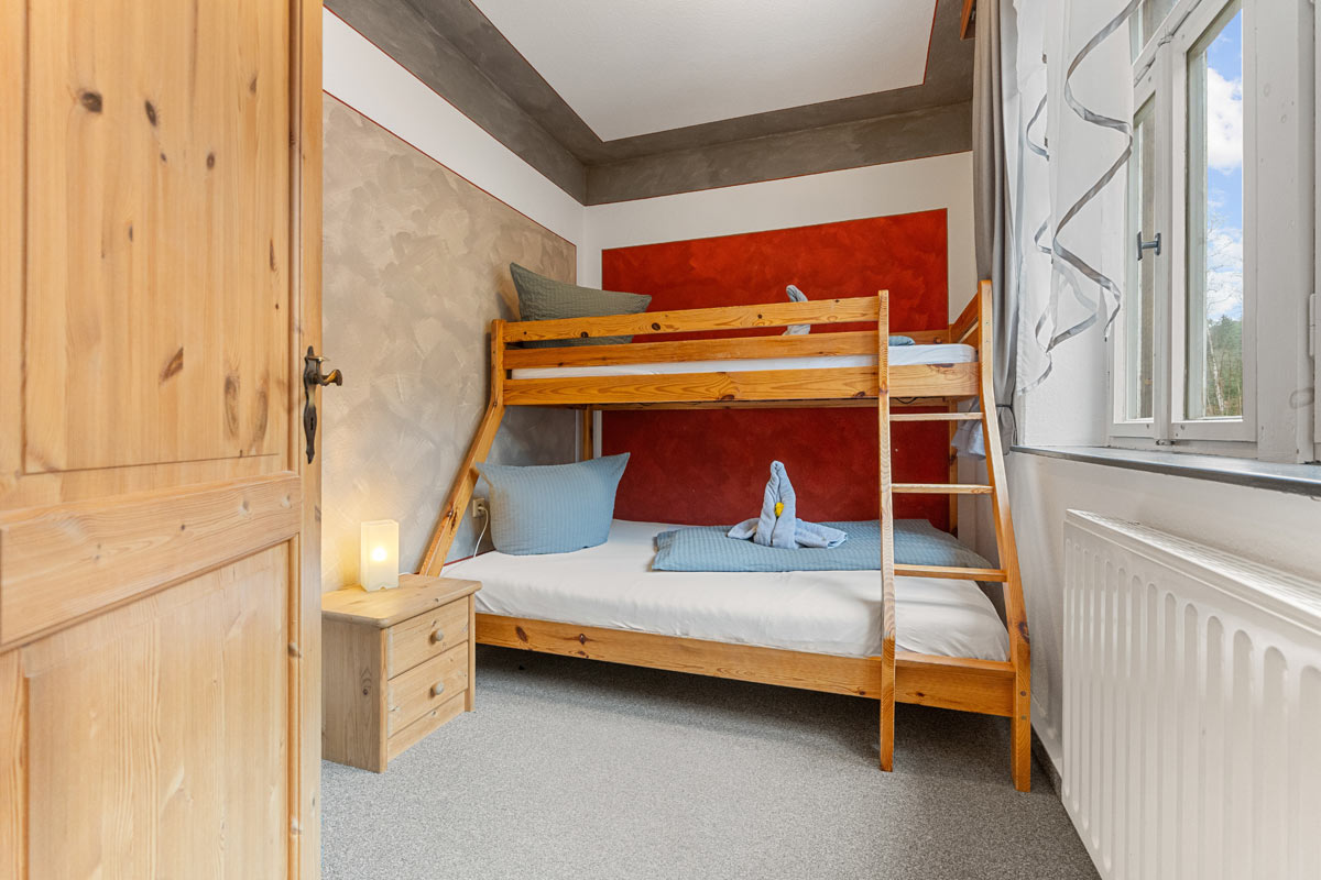 Pension Schrammsteinbaude – Familienzimmer mit Balkon – Stockbett Blick in ein helles Zimmer mit Naturholzoptik und Stockbett.