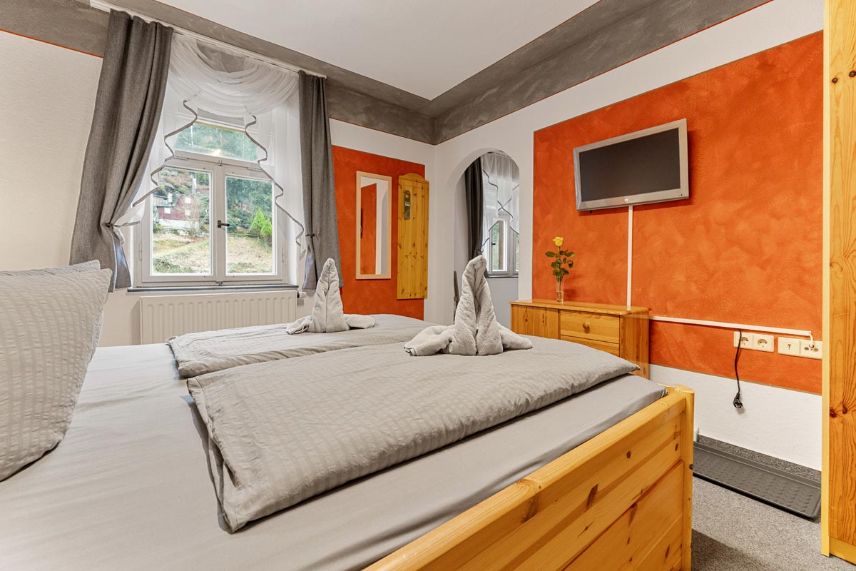 Pension Schrammsteinbaude – Familienzimmer ohne Balkon mit Doppelbett und Flat-TV Blick in ein helles Zimmer mit Naturholzoptik, Doppelbett und Flat-TV an der Wand.