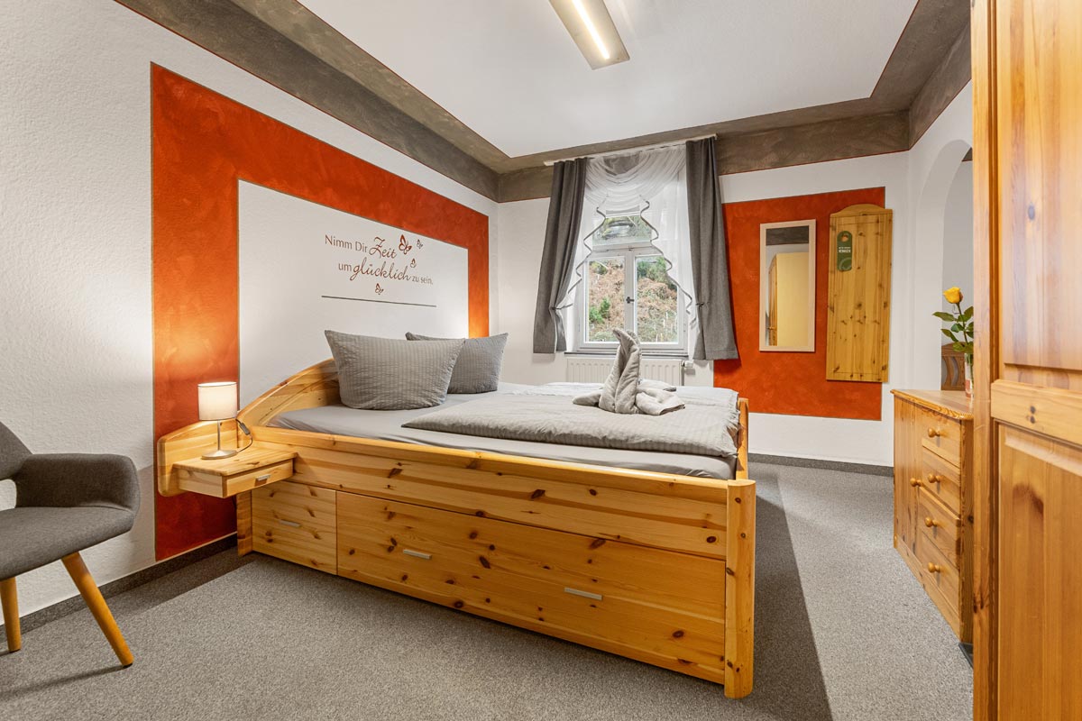 Pension Schrammsteinbaude – Familienzimmer ohne Balkon mit Doppelbett Blick in ein helles Zimmer mit Naturholzoptik, Doppelbett, Sitzgelegenheit und Wandspruch.