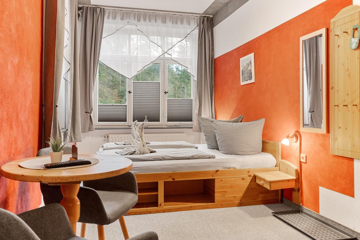 Blick in ein helles Zimmer mit Naturholzoptik, Doppelbett, Sitzgelegenheit und Blick ins Grüne.