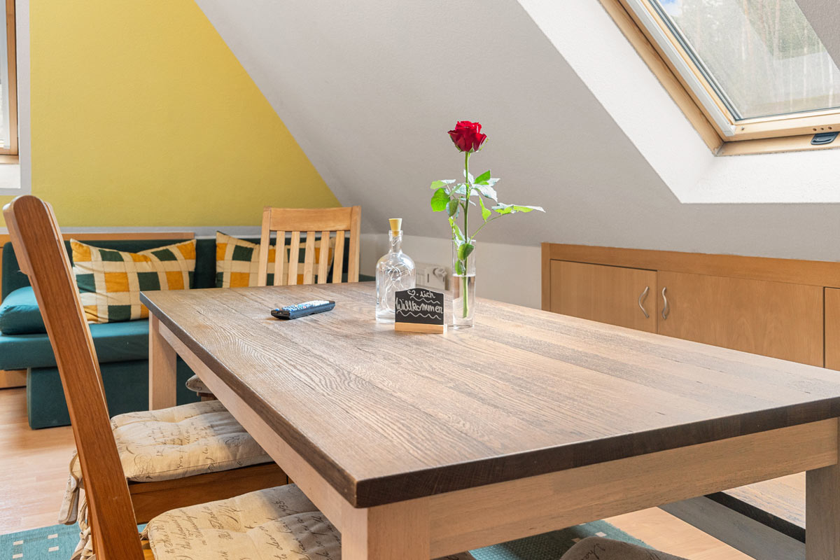 Blick in ein helles Zimmer im Dachgeschoss mit Naturholzoptik, Sofa und Esstisch.