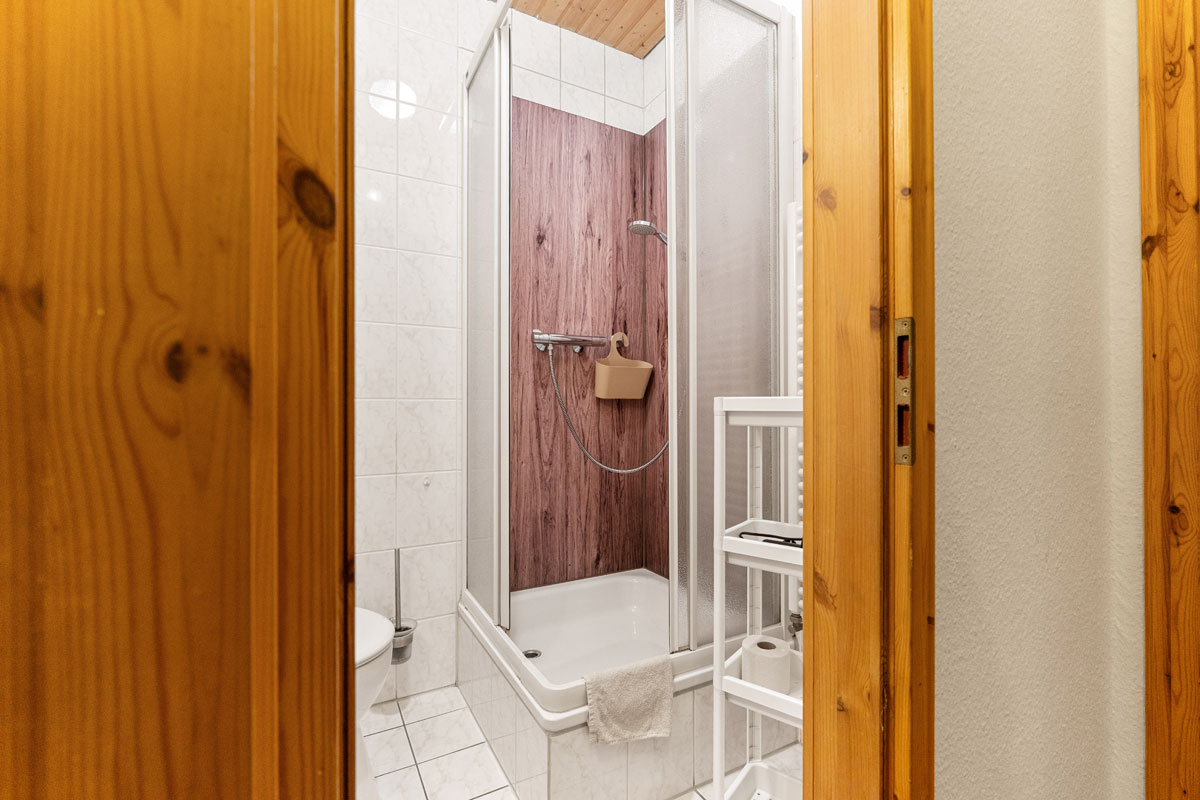 Blick in ein fensterloses Badezimmer mit weißen Fliesen, Dusche und WC.